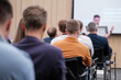 © Anton Gvozdikov - Group of people attending a tech conference, listening to a speaker giving a presentation with focus on the audience.
