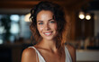 © imagineRbc - A closeup portrait of a woman with curly brown hair and blue eyes, smiling happily. She is wearing a white tank top and is standing indoors