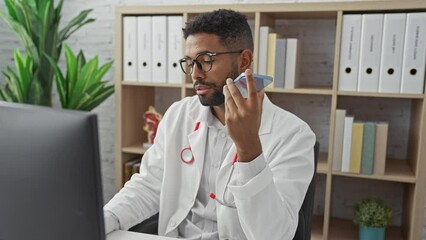 Sticker - African american doctor in lab coat using smartphone and computer in clinic office