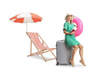 Sticker - Young woman sitting on a suitcase and holding a passport and a swimming ring next to a beach chair