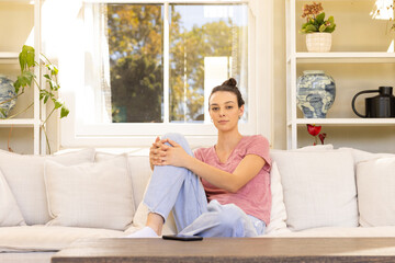 Sitting on couch, young woman relaxing at home in casual attire