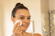 © WavebreakMediaMicro - Smiling woman applying facial cleanser with cotton pad in bathroom