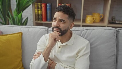 Poster - Young hispanic man with pensive expression, thinking and smiling at home, hand on chin in a display of thoughtfulness amidst doubt and question