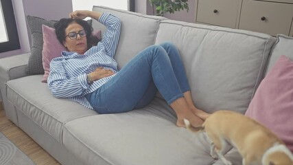 Sticker - Mature woman in glasses, resting on a couch in a cozy living room with a chihuahua dog wandering around.