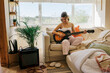 © BONNINSTUDIO/Stocksy - Woman playing electric guitar at home