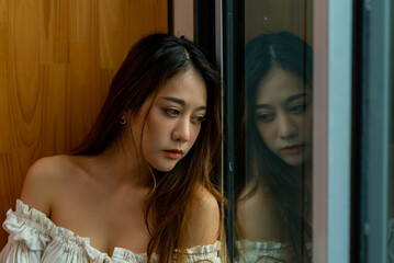 Depressed Asian woman sitting alone on the floor bedroom with hugging self and crying. Loneliness sad girl thinking grief trouble life problems. Negative emotion and people mental health concept.