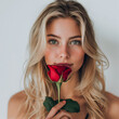 © Patcharee - Close-up of a beautiful woman with long blonde hair, smiling, holding a red rose.