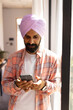 © Wavebreak Media - Using smartphone, Indian man in turban standing by window at home