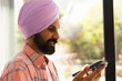 © Wavebreak Media - Using smartphone, man in turban smiling and looking at screen indoors