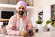 © Wavebreak Media - Holding smartphone, man in turban standing in modern home interior