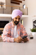 © Wavebreak Media - Using smartphone, man in turban sitting at home, smiling and texting