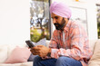 © Wavebreak Media - Using smartphone, man in turban sitting on couch at home, concentrating