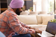© Wavebreak Media - Typing on laptop, man in turban working from home on couch