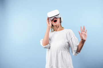 Wall Mural - Happy woman surprised or excited while looking though VR glasses and standing at blue background. Caucasian girl with white pajamas using visual reality goggles to connect with metaverse. Contraption.