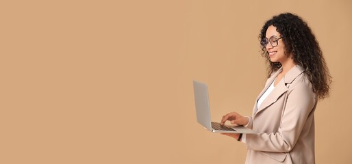 Wall Mural - Young African-American businesswoman holding modern laptop on beige background with space for text