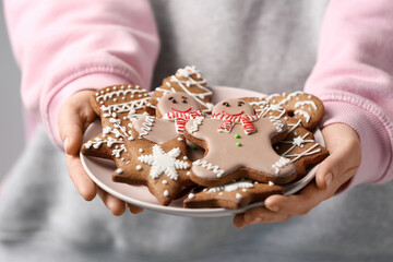 Wall Mural - Woman holding plate with Christmas gingerbread cookies on grey background, closeup view