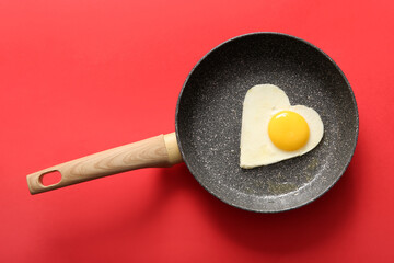 Wall Mural - Frying pan with tasty fried egg in shape of heart on red background