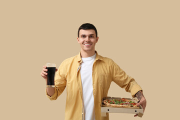 Wall Mural - Young man holding cardboard box with tasty pizza and glass of cola on beige background