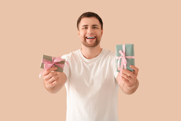 Wall Mural - Handsome happy young man with gift boxes on beige background