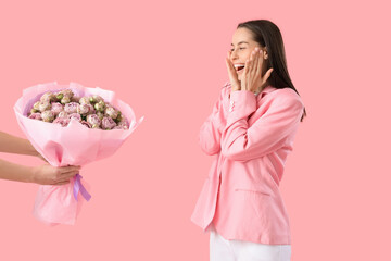 Wall Mural - Surprised young woman receiving bouquet of beautiful roses on pink background