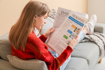 Poster - Beautiful young woman reading newspaper on sofa near color wall