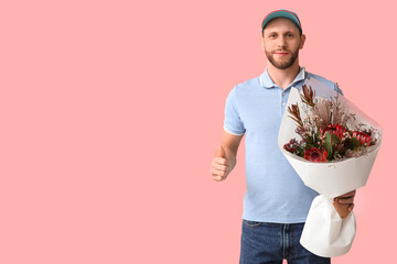 Wall Mural - Young delivery man with bouquet of beautiful flowers showing thumb-up gesture on pink background