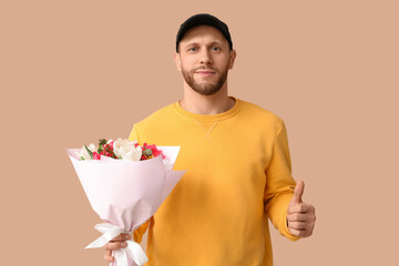 Wall Mural - Young delivery man with bouquet of beautiful tulips showing thumb-up gesture on brown background