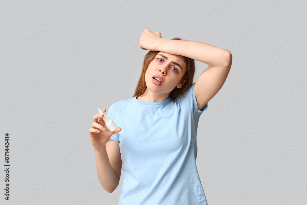 Young woman with nasal spray suffering from allergy on grey background