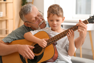 Wall Mural - Grandfather teaching his cute little grandson playing guitar at home