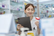 © eakgrungenerd - woman pharmacists are selecting medications for patients online via tablet in drug store. Drug seller use tablet holding medicine bottle check for information before sending to patient.
