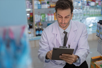 Wall Mural - man pharmacists are selecting medications for patients online via tablet in drug store. Drug seller use tablet check for information before sending to patient.