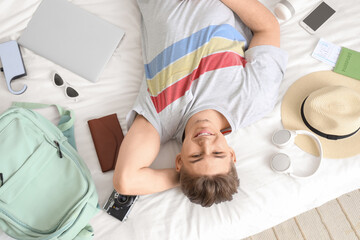 Sticker - Male tourist with travel accessories lying on bed in hotel room, top view