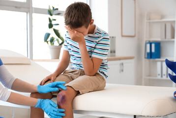 Wall Mural - Crying little boy with bruised knee visiting doctor in clinic