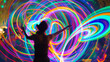 © XaMaps - Person spinning LED light poi during a festival at dusk creating colorful long exposure trails in the air.