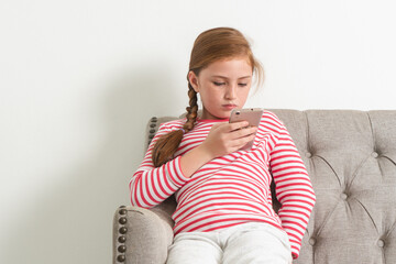 internet social addict in children concept, young girl in casual attire holding smartphone focused on device screen during relex at home.