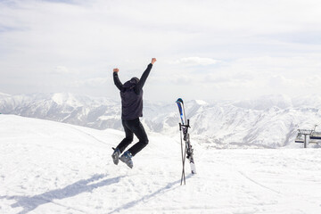 A skier jumps with his arms raised facing the mountains. The concept of active recreation in the Gudauri mountains