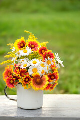 Poster - white enamel mug with colorful flowers on table in garden, natural abstract background. summer season. rustic composition with flowers. relax time. template for design