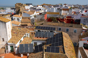 An aerial view of a small town showcasing an array of traditional terracotta rooftops equipped with modern solar panels, reflecting the blend of old and new technologies in Carmina in Andalusia