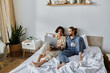 © LIGHTFIELD STUDIOS - A loving couple relaxes in bed together, enjoying coffee and browsing a laptop.