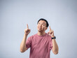© Daniel - A man in a pink shirt points upwards with both index fingers and an enthusiastic expression, as if presenting an idea or emphasizing a point. The plain light blue background highlights his animated