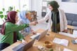 © Studio Marmellata - Three women in hijabs shaking hands at their office desk
