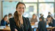© Kenny - Confident Teacher Smiling in Classroom with Students Working in the Background
