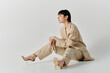 © LIGHTFIELD STUDIOS - A woman in a tan suit sits on a white background, wearing clear heels.