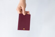 © cabuscaa - Hand holding a red passport with a blank cover and the biometric symbol on a white background