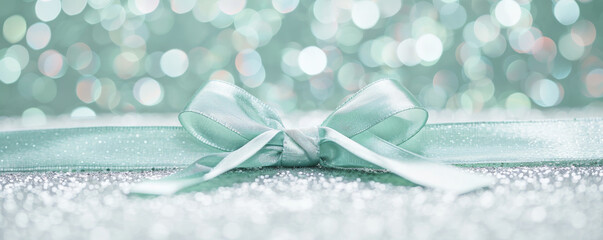 Wall Mural - A soft mint green ribbon bow on a silver glitter background. The fresh color and shimmering backdrop create a refreshing and elegant look.
