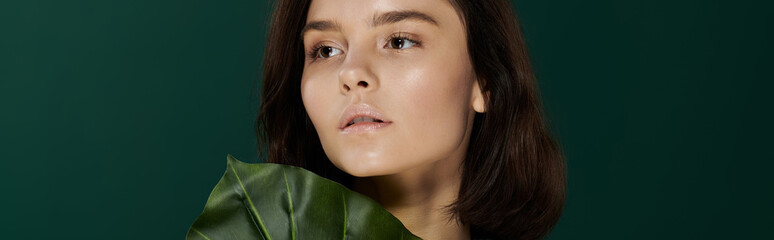 Wall Mural - A portrait of a woman with a soft gaze, posing against a backdrop of vibrant green foliage.