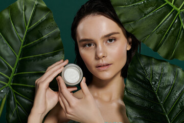 Wall Mural - A woman poses with a cream jar in front of a vibrant green backdrop.