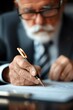 © Mind - Elderly man in suit signing a document with a pen. Close-up of his hand, focusing on the pen and paper.