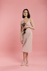 Wall Mural - A woman in a pink dress poses with a rose in front of a pink background.