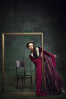 © master1305 - Portrait of curious elegant young woman, royal person peek out picture frame with interest against dark green background. Mystery of future. Concept of history, comparison of eras, remake